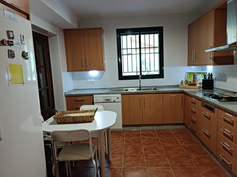 Cocina equipada con muebles de madera, encimera de granito, ventana con reja y mesa pequeña