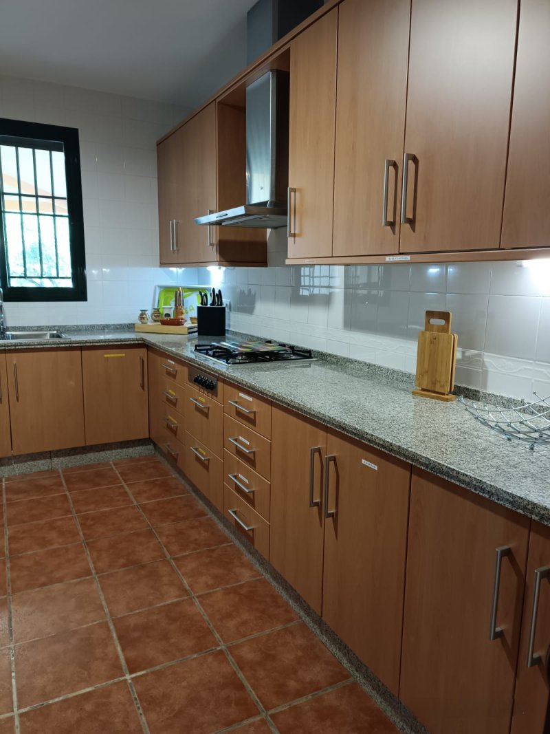 Cocina amplia con muebles de madera, encimera de granito y suelo cerámico.