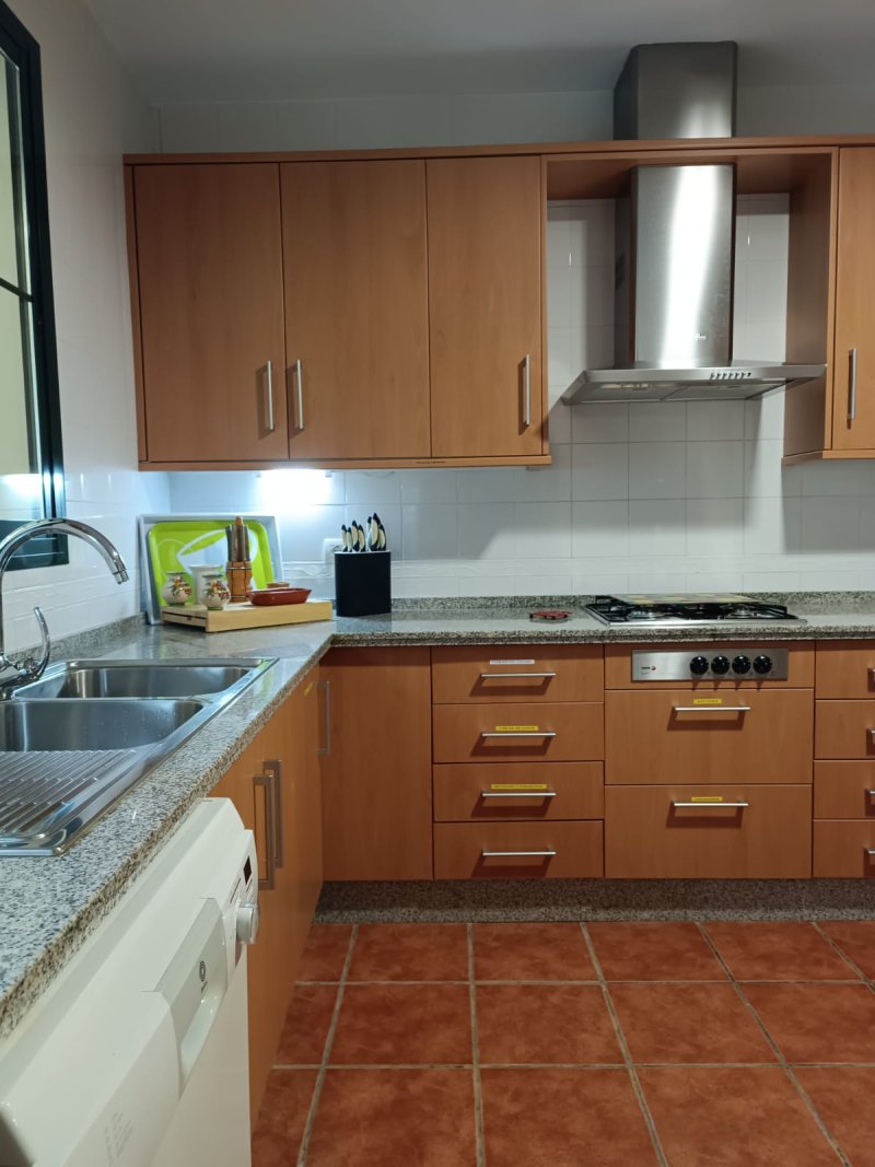 Cocina equipada con muebles de madera, encimera de granito, vitrocerámica y campana extractora.