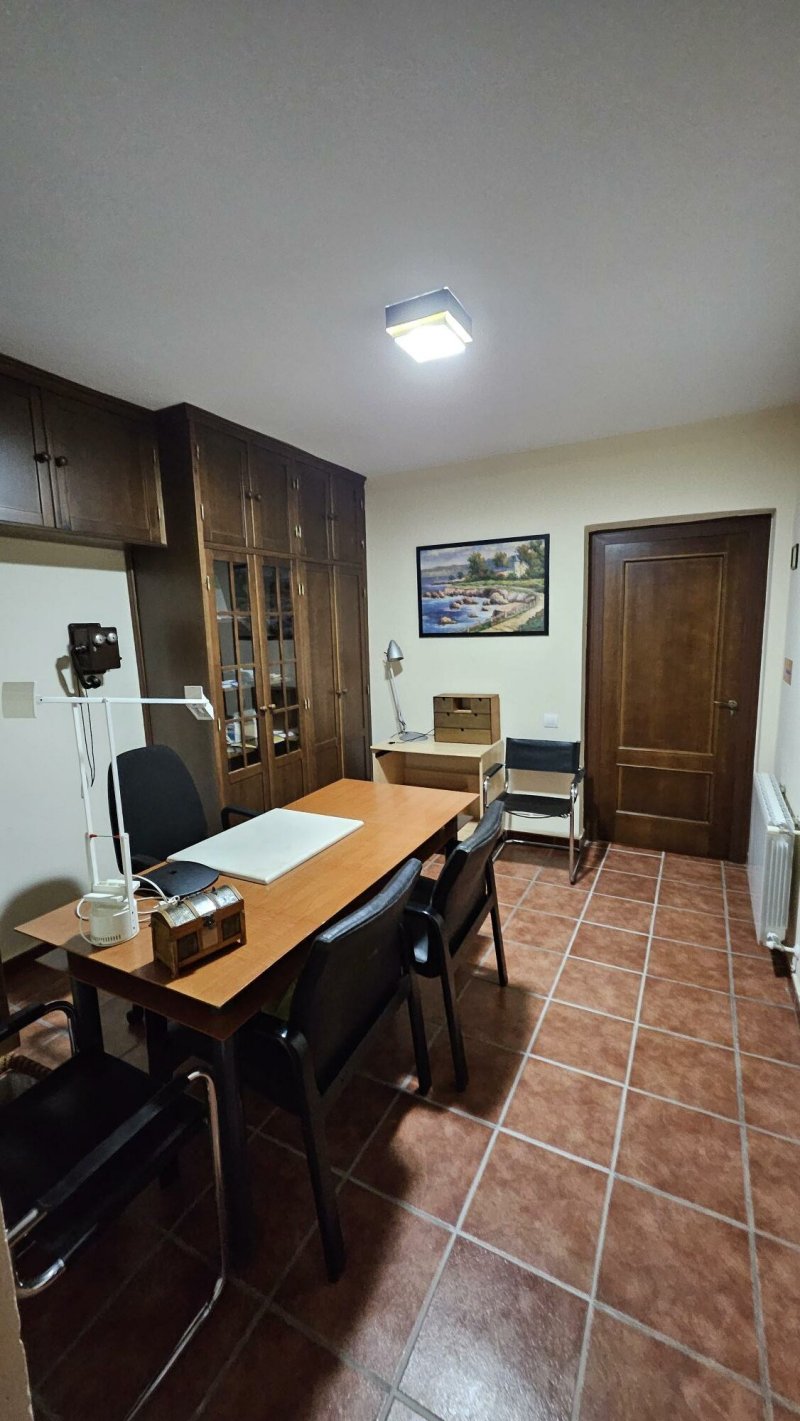 Despacho rural con escritorio de madera, sillas negras, armario clásico y radiador.