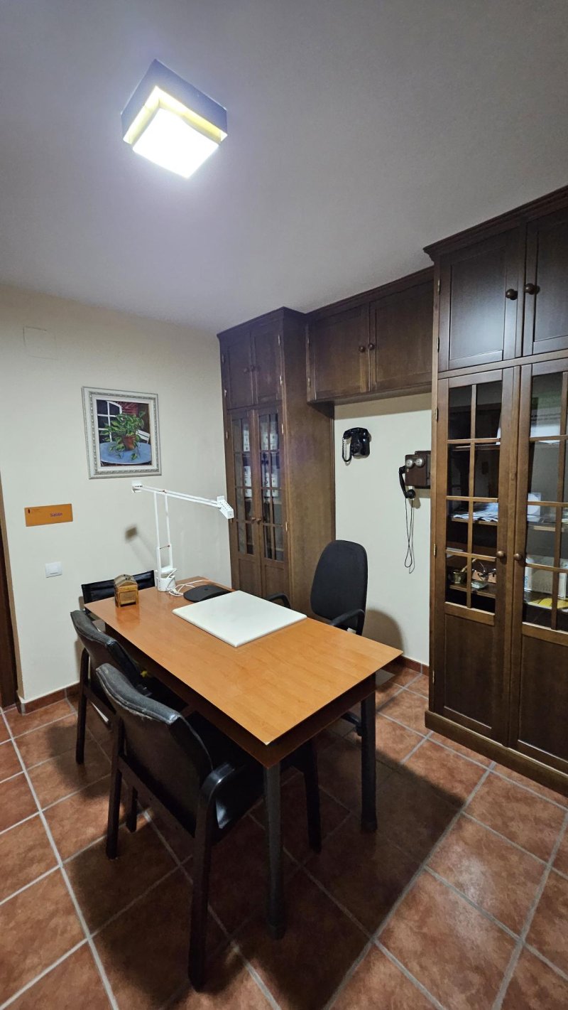 Oficina rural con mesa de madera, sillas, armarios oscuros y teléfono antiguo de pared.