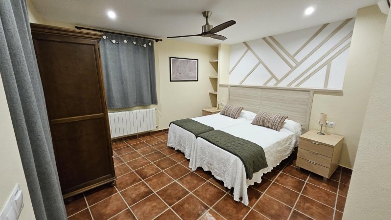 Dormitorio con dos camas individuales, armario de madera, suelo de terracota y ventilador de techo