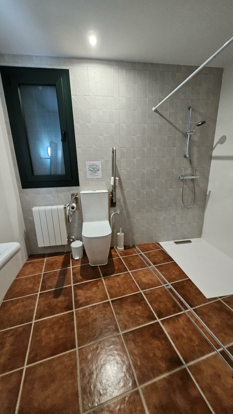 Baño adaptado con ducha a ras de suelo, inodoro con barras de apoyo y ventana