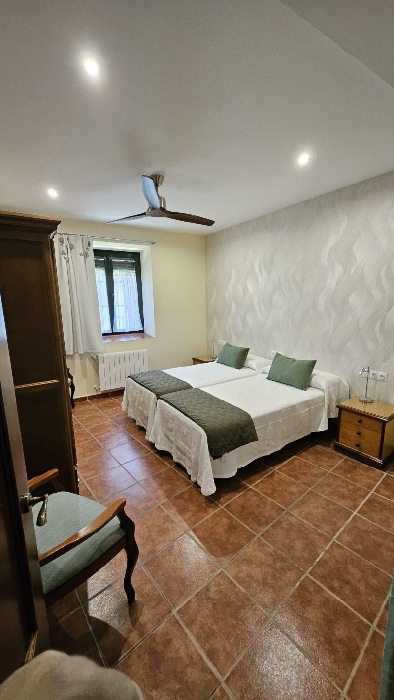 Habitación doble con dos camas, suelo de barro, papel pintado gris y ventilador de techo