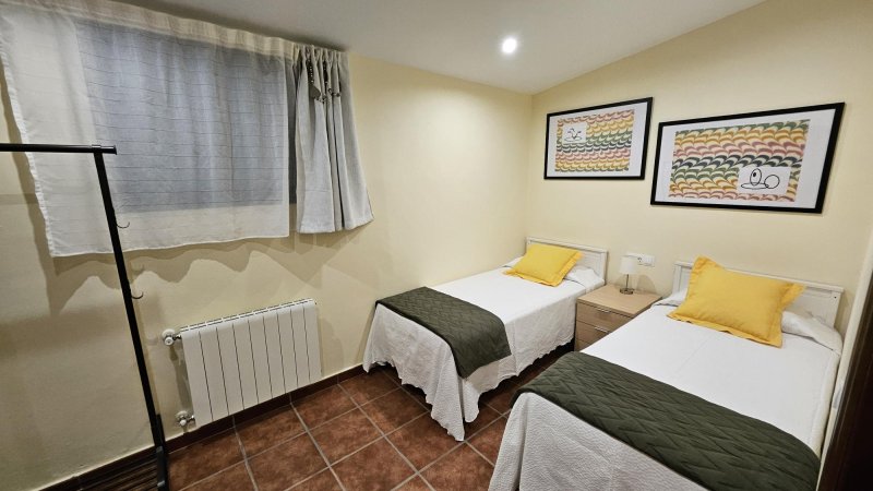 Habitación doble con dos camas individuales, almohadas amarillas y radiador blanco