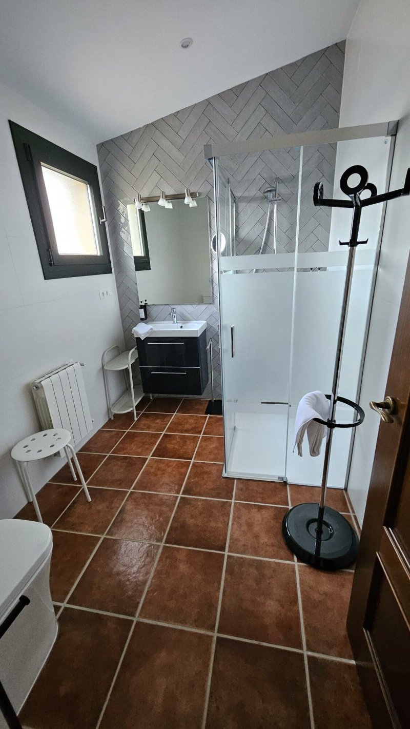 Baño moderno con ducha de cristal, lavabo negro, suelo de barro y toallero