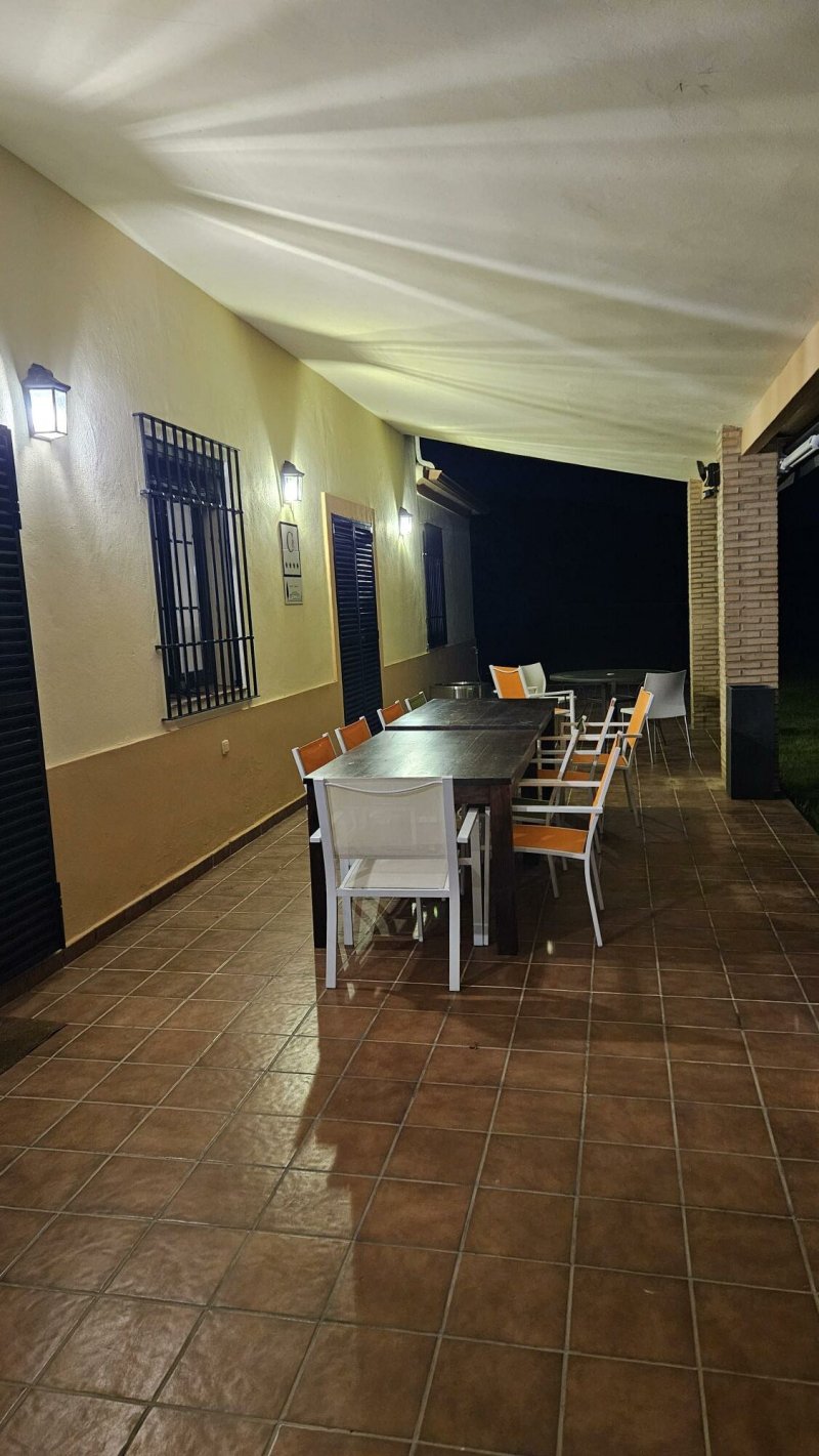 Terraza cubierta nocturna con mesa larga y sillas naranjas en casa rural