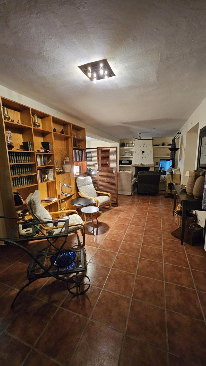 Salón rústico con estantería de madera, sillones, chimenea y suelo de terracota