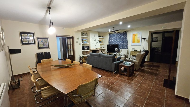 Salón comedor amplio con mesa de madera, sofá gris y televisión.