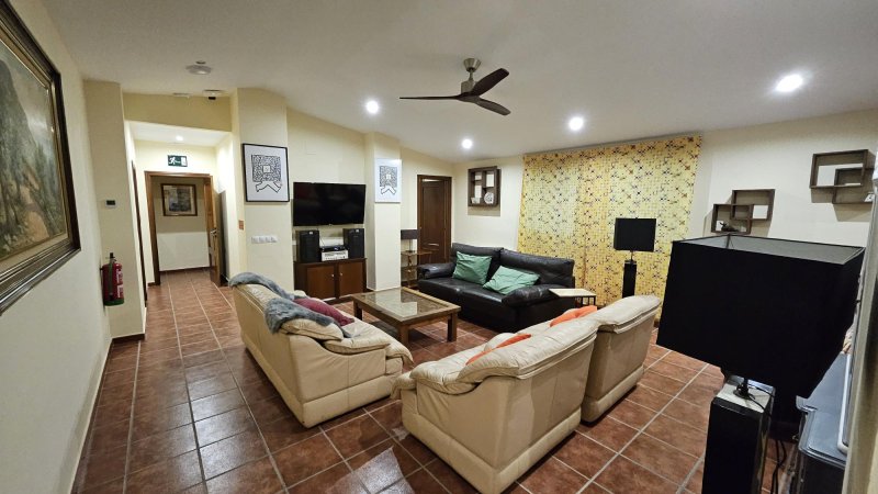 Salón amplio con sofás de piel, TV, suelo de terracota y ventilador de techo