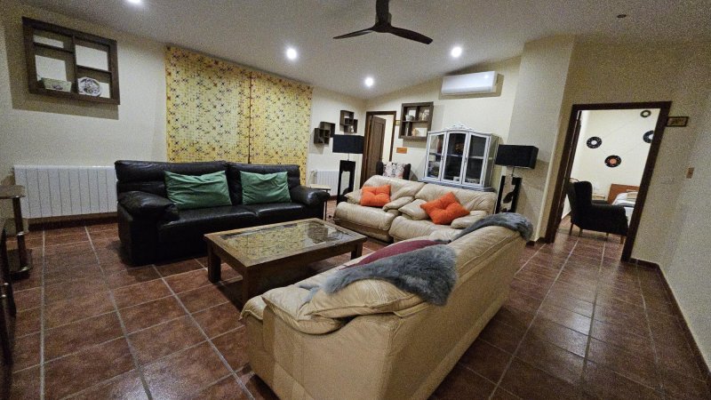 Amplio salón rural con tres sofás de cuero, mesa de cristal y ventilador de techo