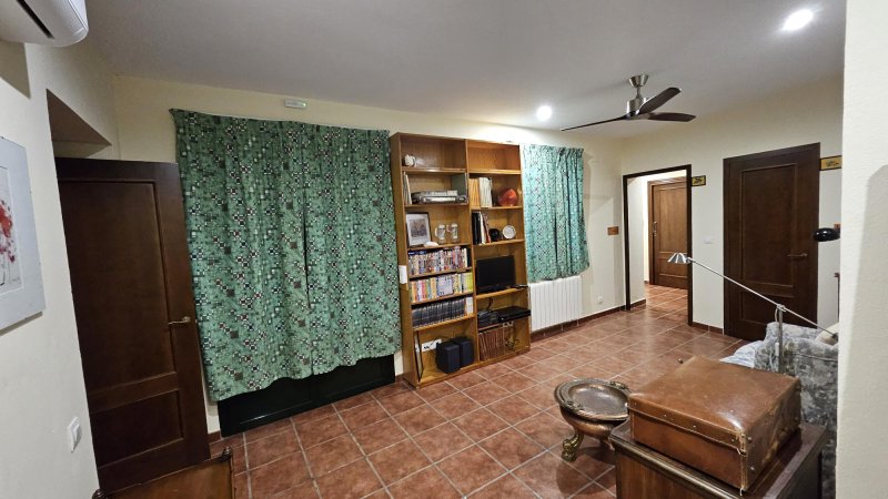 Salón con librería de madera, cortinas verdes, suelo de baldosa y ventilador de techo
