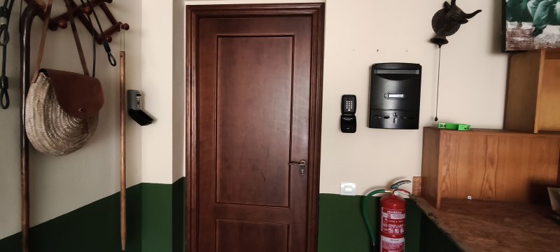 Entrada de casa rural con puerta de madera, buzón, teclado digital y extintor rojo.