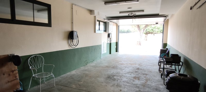 Garaje amplio con cargador eléctrico, paredes bicolores verde y blanco, puerta levadiza abierta.