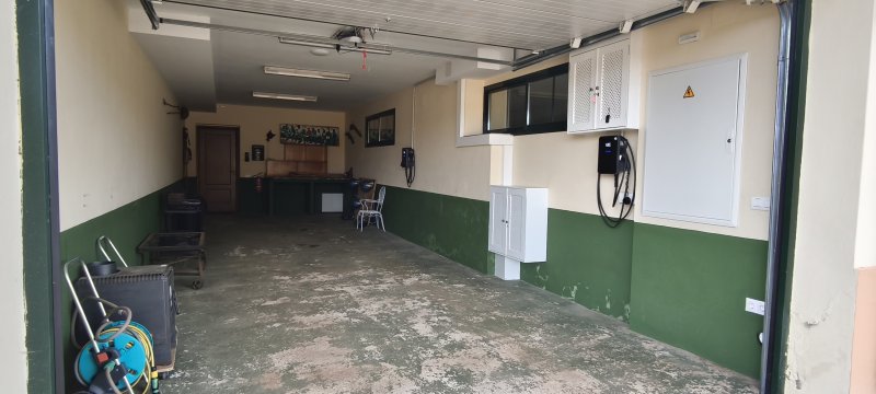 Garaje amplio con paredes verdes, cargador eléctrico para vehículos y zona de trabajo